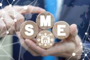 A man holding four round wooden blocks, in which the letters S , M, E are mentioned in white color, is a small mediumsized enterprises concept business.