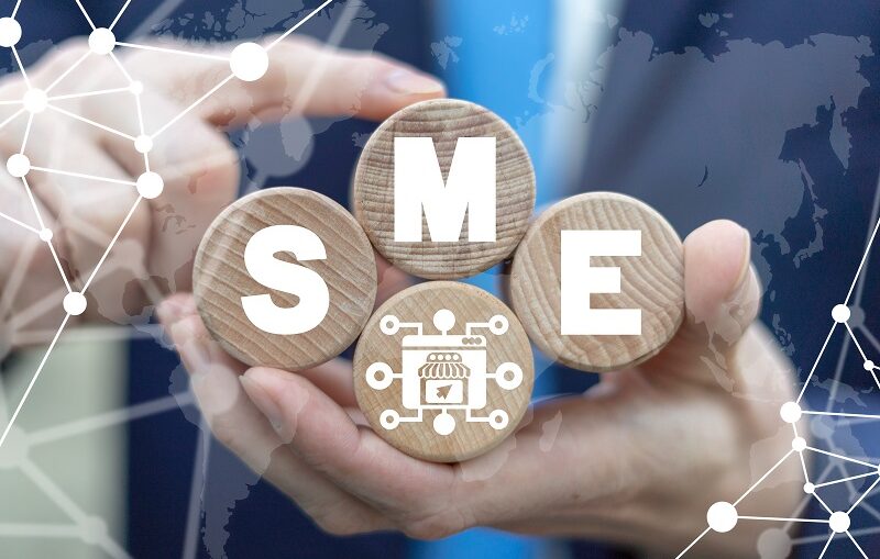 A man holding four round wooden blocks, in which the letters S , M, E are mentioned in white color, is a small mediumsized enterprises concept business.